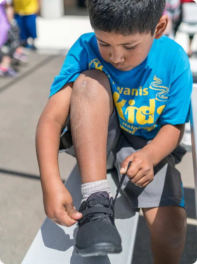 Een jongen van Save the Children die zijn schoenen strikt.